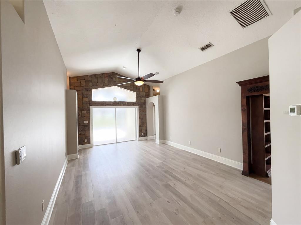 A living room features light wood-look flooring, a stone accent wall, and a vaulted ceiling — 3028 SAMOSA HILL CIRCLE, CLERMONT, FL