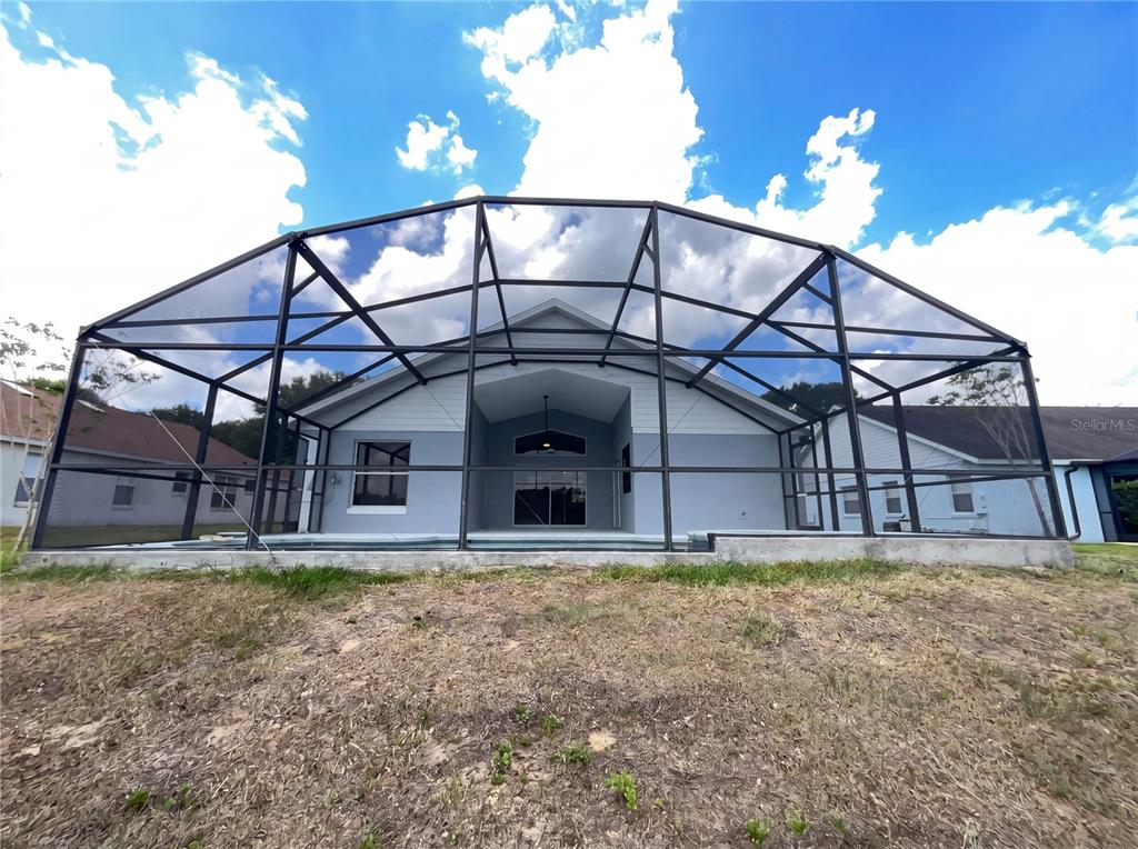 A rear view of a house with a screened-in pool enclosure and a grassy yard — 3028 SAMOSA HILL CIRCLE, CLERMONT, FL