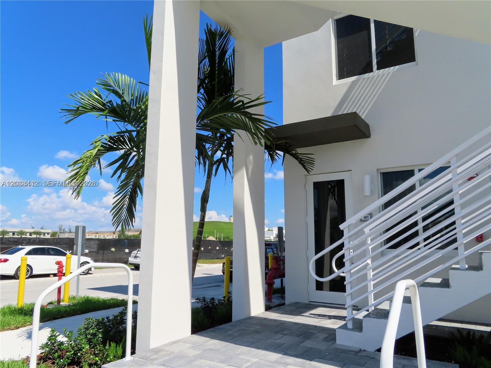A white building exterior features a staircase, a palm tree, and a paved walkway — 6401 NW 103rd Pl # 101, Doral FL 33178, DORAL, FL