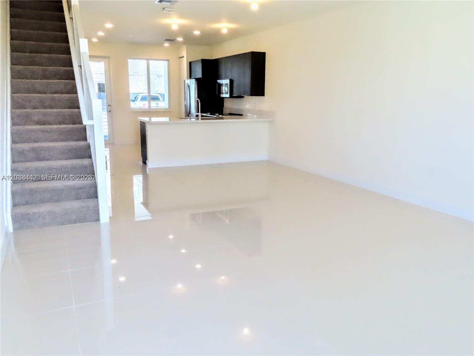 An open-concept living area features white tile floors, a carpeted staircase, and a modern kitchen — 6401 NW 103rd Pl # 101, Doral FL 33178, DORAL, FL