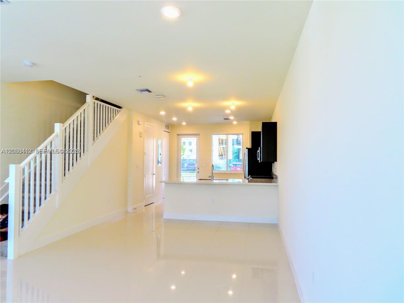 A bright, open-concept living area features a staircase, tiled floors, and a kitchen with dark cabinets — 6401 NW 103rd Pl # 101, Doral FL 33178, DORAL, FL