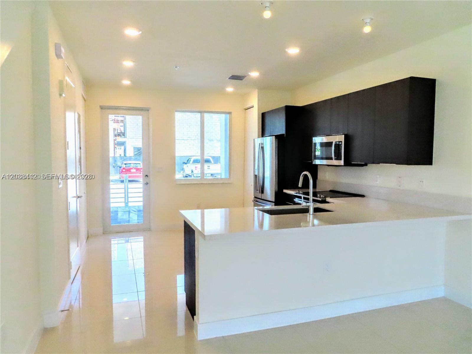 A modern kitchen features dark cabinetry, white countertops, stainless steel appliances, and glossy tile floors — 6401 NW 103rd Pl # 101, Doral FL 33178, DORAL, FL
