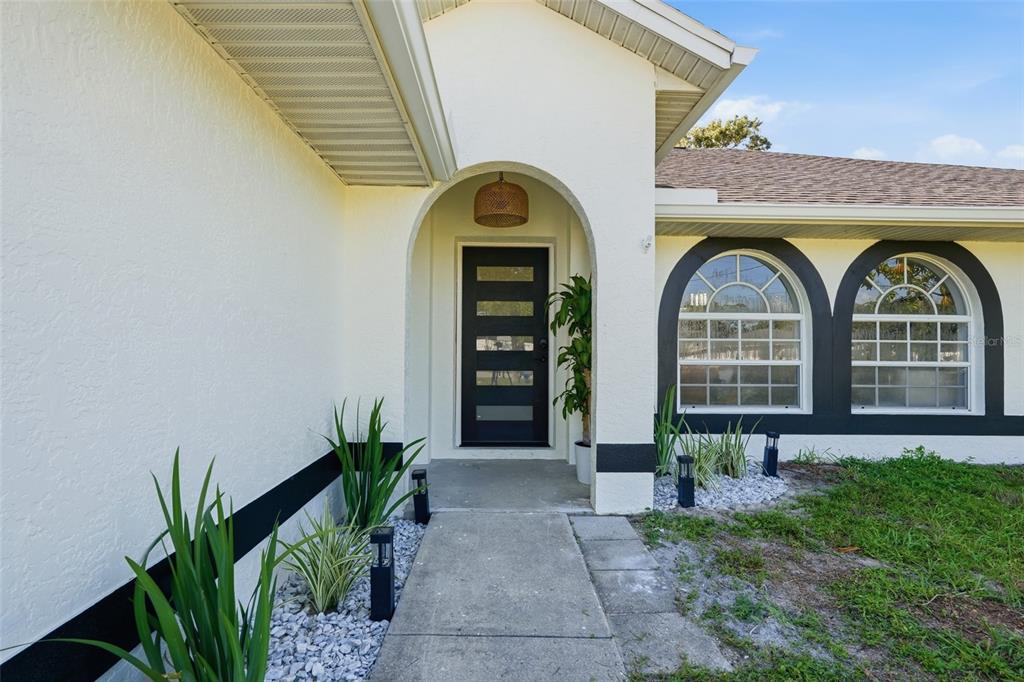 The exterior of a house features a white stucco facade, a black front door, and arched windows — 4850 S SALFORD BOULEVARD, NORTH PORT, FL