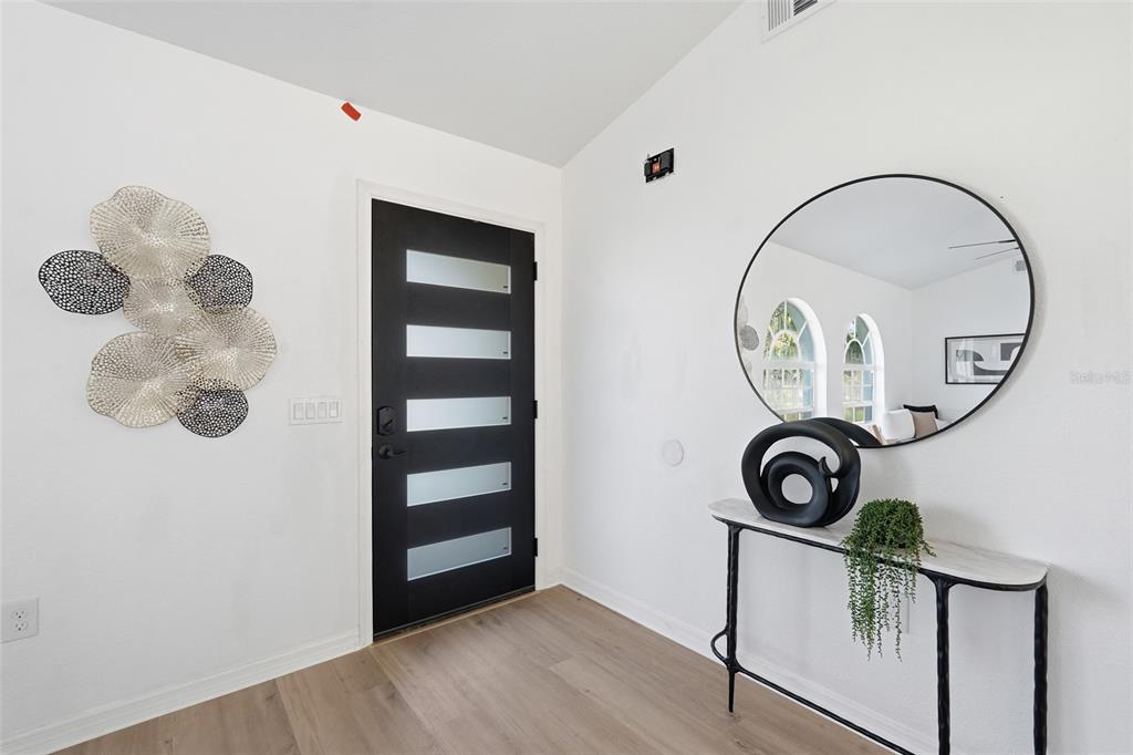 An entryway features a black door with frosted glass panels, a round mirror, and console table — 4850 S SALFORD BOULEVARD, NORTH PORT, FL