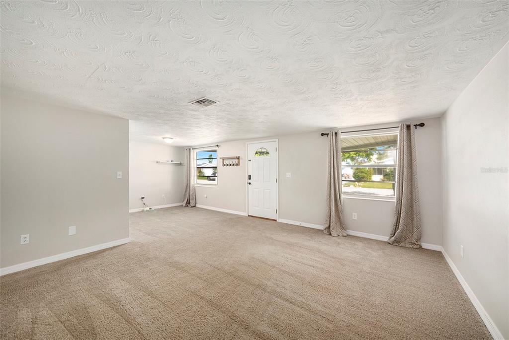 A carpeted living room with a textured ceiling, white walls, and two windows with curtains — 3510 ALLANDALE DRIVE, HOLIDAY, FL
