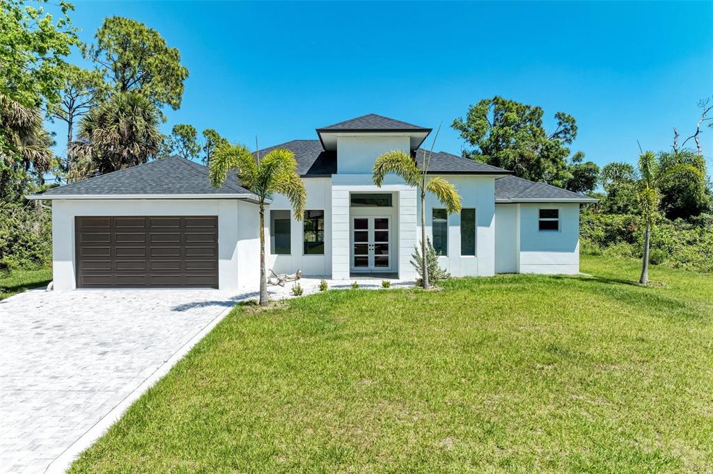 A modern white single-story house with a dark roof, garage, and palm trees — 3260 ABBOTSFORD STREET, NORTH PORT, FL