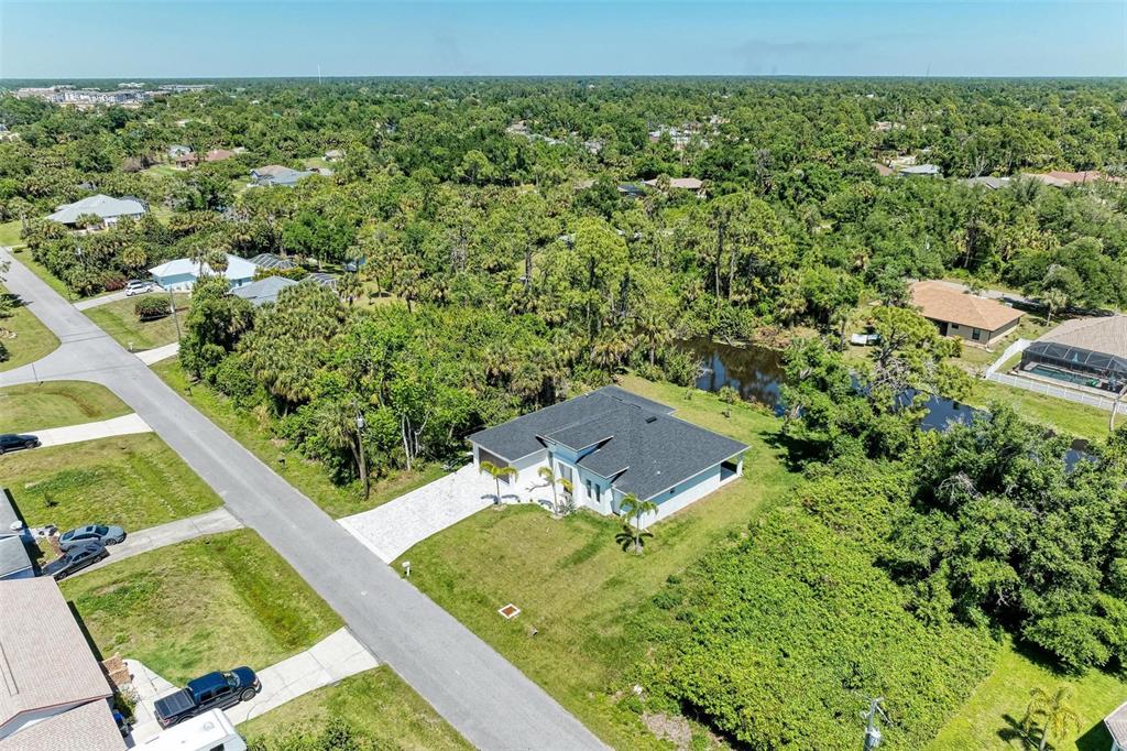 An aerial view shows a single-story house with a dark roof and a small pond — 3260 ABBOTSFORD STREET, NORTH PORT, FL