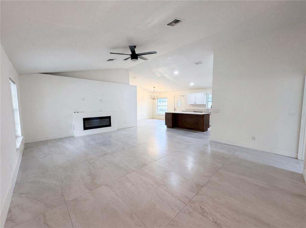 A spacious living room features large light-colored floor tiles, a fireplace, and an open kitchen — 11200 ROSEHILL DRIVE, CLERMONT, FL
