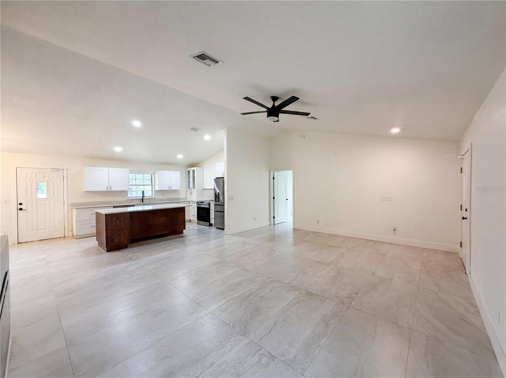 An open-concept kitchen and living area features white cabinetry, a dark wood island, and tile flooring — 11200 ROSEHILL DRIVE, CLERMONT, FL