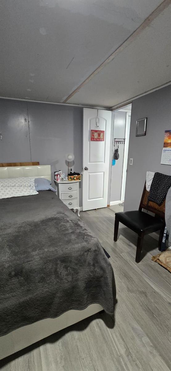 A bedroom features a bed with a gray blanket, a white nightstand, and a black chair — 100 SE 6th Ave, Homestead FL 33030, HOMESTEAD, FL