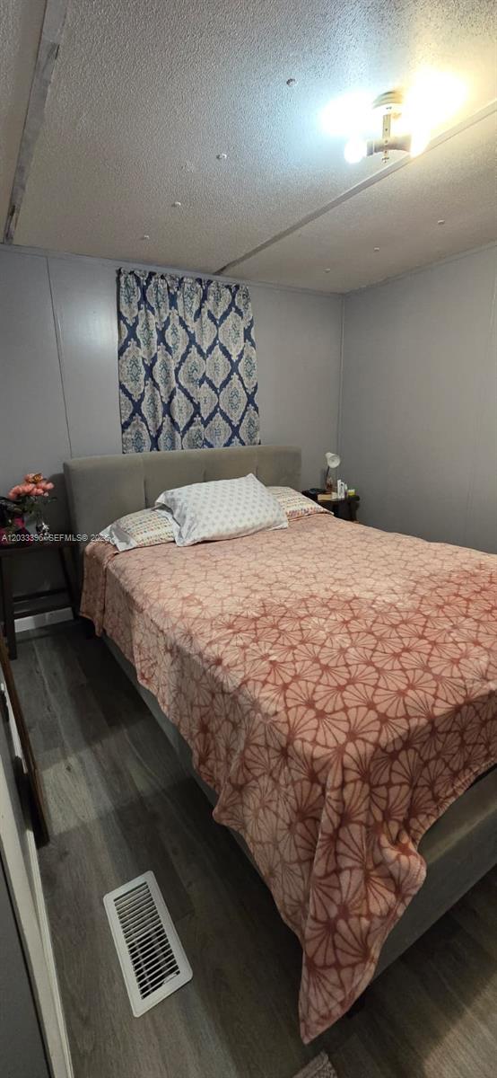 A bedroom features a gray upholstered bed, patterned bedding, light-colored walls, and wood-look flooring — 100 SE 6th Ave, Homestead FL 33030, HOMESTEAD, FL