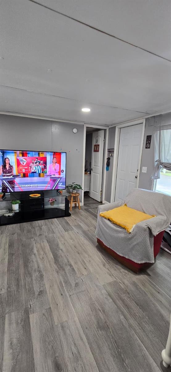 A living room features gray wood-look flooring, a television on a stand, and an armchair — 100 SE 6th Ave, Homestead FL 33030, HOMESTEAD, FL