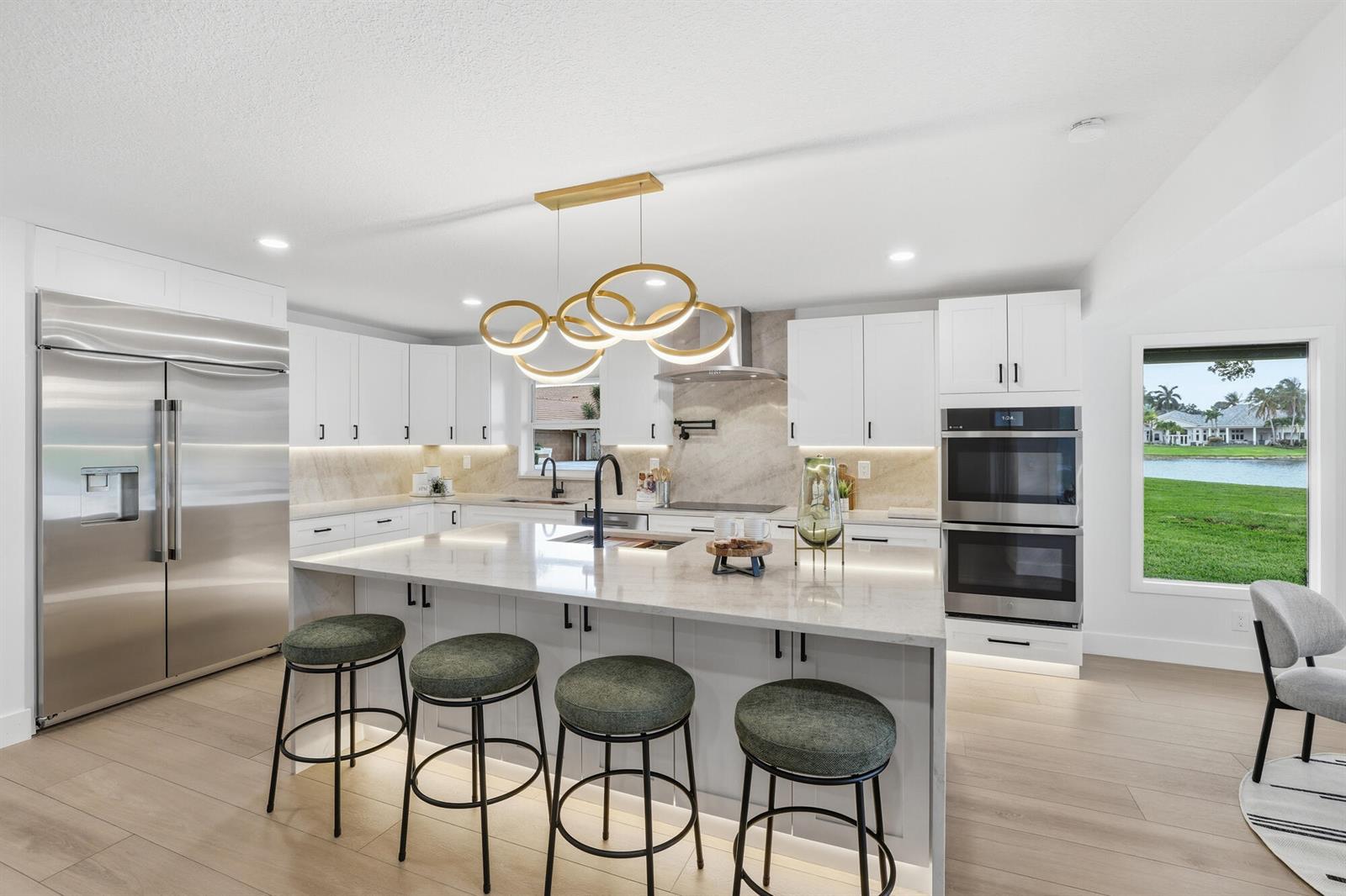A modern white kitchen features a large island with bar stools and a scenic lake view — 7411 Dover Lane, Parkland FL 33067, PARKLAND, FL