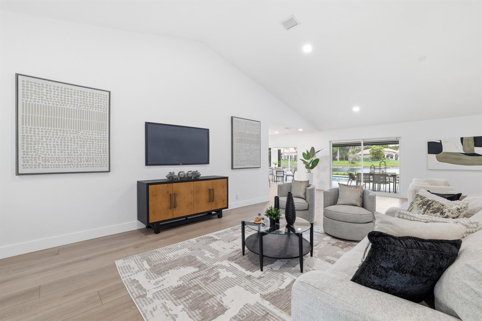 A bright living room features a vaulted ceiling, light wood floors, and a view of a pool — 7411 Dover Lane, Parkland FL 33067, PARKLAND, FL