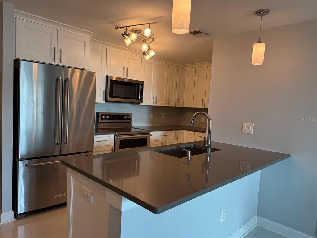 A modern kitchen features white cabinetry, stainless steel appliances, and a dark quartz island countertop — 345 BAYSHORE BOULEVARD UNIT 1102, TAMPA, FL