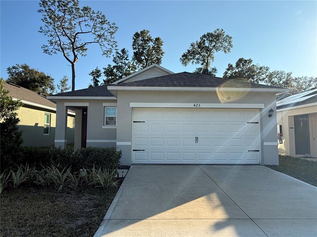 A single-story house with a white garage door, beige stucco exterior, and a concrete driveway — 423 PELHAM PARK DRIVE, DELAND, FL