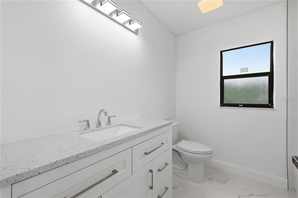 A modern bathroom features a white vanity with a speckled countertop, toilet, and window — 3506 FAIRWAY FOREST DRIVE, PALM HARBOR, FL