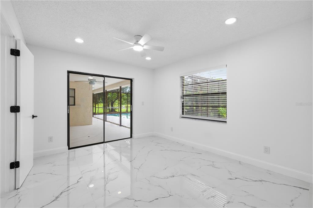 A bright bedroom features white walls, marble-patterned tile flooring, a ceiling fan, and sliding glass doors — 3506 FAIRWAY FOREST DRIVE, PALM HARBOR, FL