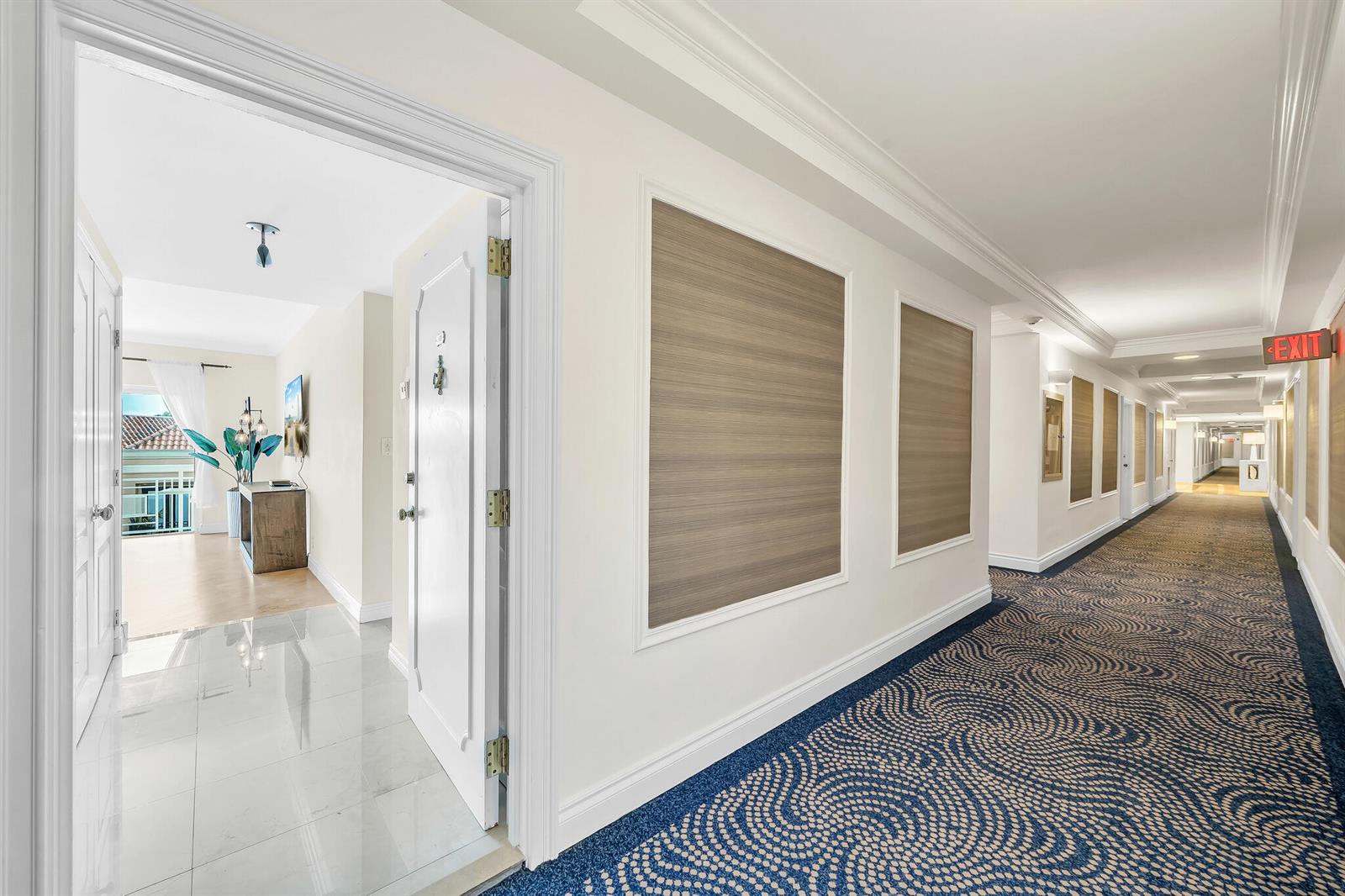 A hallway with patterned carpet leads to a white door opening into a bright apartment — 250 N Bradley Place # 402, Palm Beach FL 33480, PALM BEACH, FL
