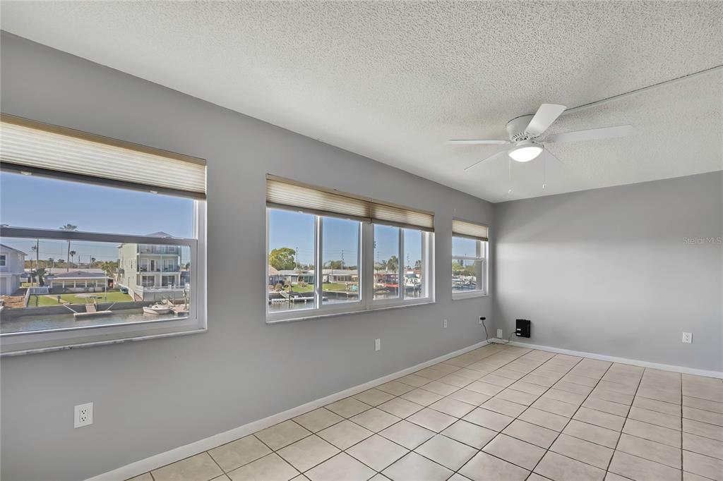 A bright room with tiled floors, a ceiling fan, and large windows overlooking a canal — 4452 GARNET DRIVE UNIT 203, NEW PORT RICHEY, FL