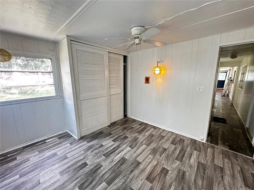 A bedroom features wood-look flooring, white paneled walls, a ceiling fan, and louvered closet doors — 817 PARKS STREET, WILDWOOD, FL