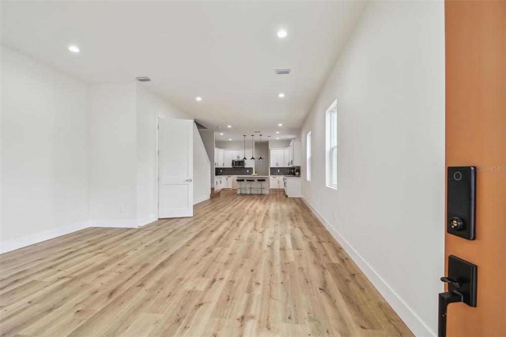 An open-concept living area with light wood flooring leads to a kitchen with white cabinets — 3455 17TH AVENUE S, ST PETERSBURG, FL