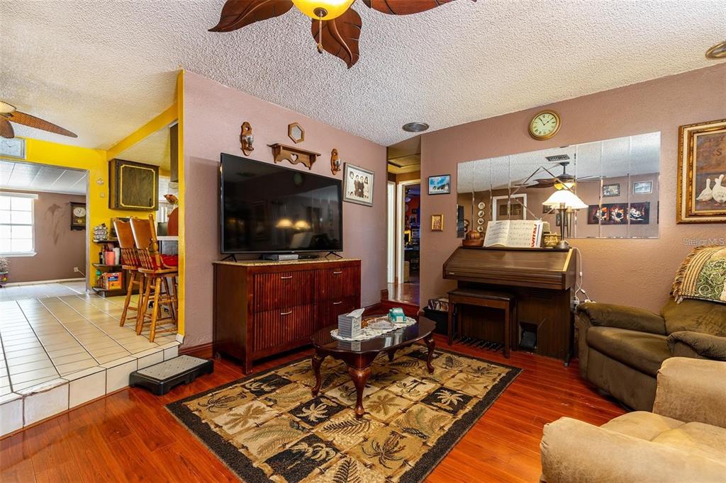 A living room features a television on a wooden cabinet, a piano, and hardwood floors — 12095 102ND AVENUE, SEMINOLE, FL