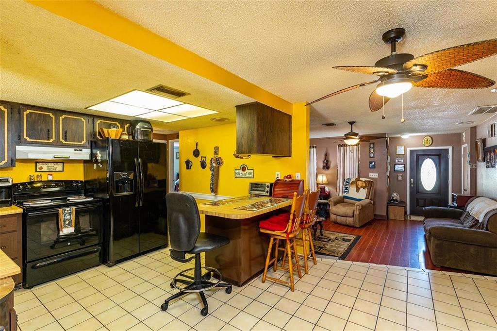 A kitchen with yellow walls and black appliances opens into a living room area — 12095 102ND AVENUE, SEMINOLE, FL