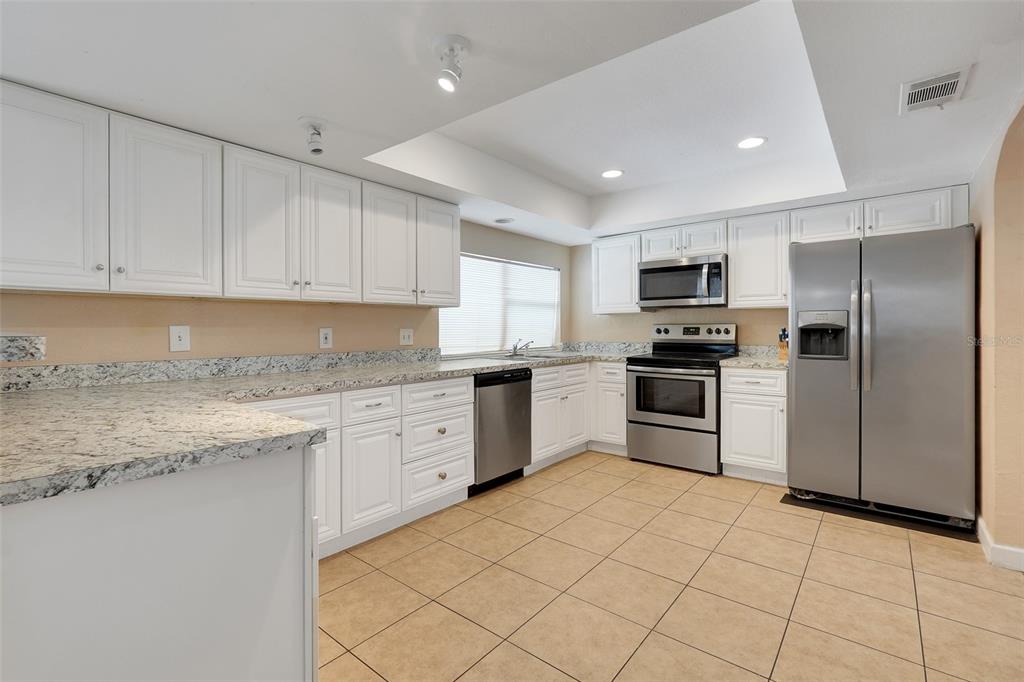 A kitchen featuring white cabinets, granite countertops, stainless steel appliances, and tan tile flooring — 3874 TAM DRIVE, ORLANDO, FL