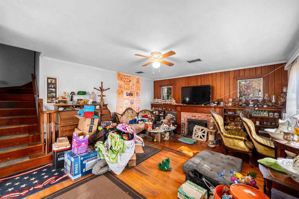 A cluttered living room features wood-paneled walls, a brick fireplace, and a wooden staircase — 9602 RIPLEY ROAD, THONOTOSASSA, FL