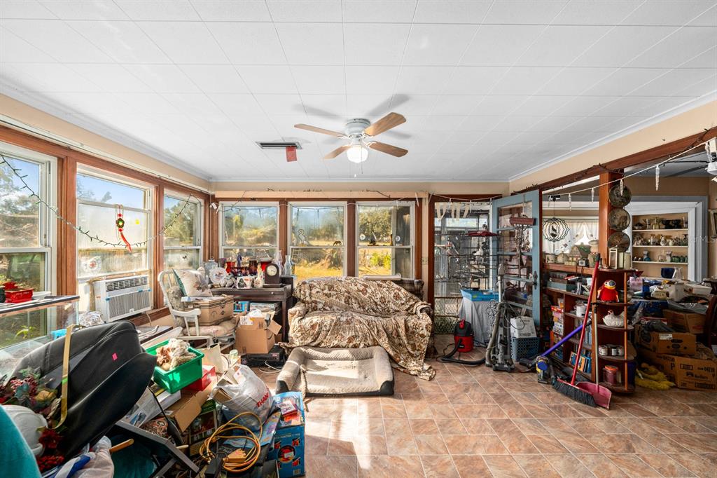 A sunroom with tile flooring, a ceiling fan, and large windows overlooking a grassy yard — 9602 RIPLEY ROAD, THONOTOSASSA, FL