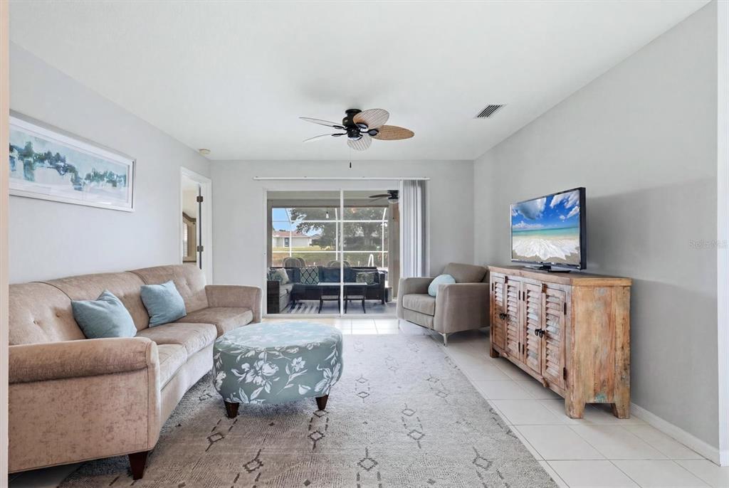 A living room features a beige sofa, patterned ottoman, wooden media console, and sliding glass doors — 175 BUNKER ROAD, ROTONDA WEST, FL