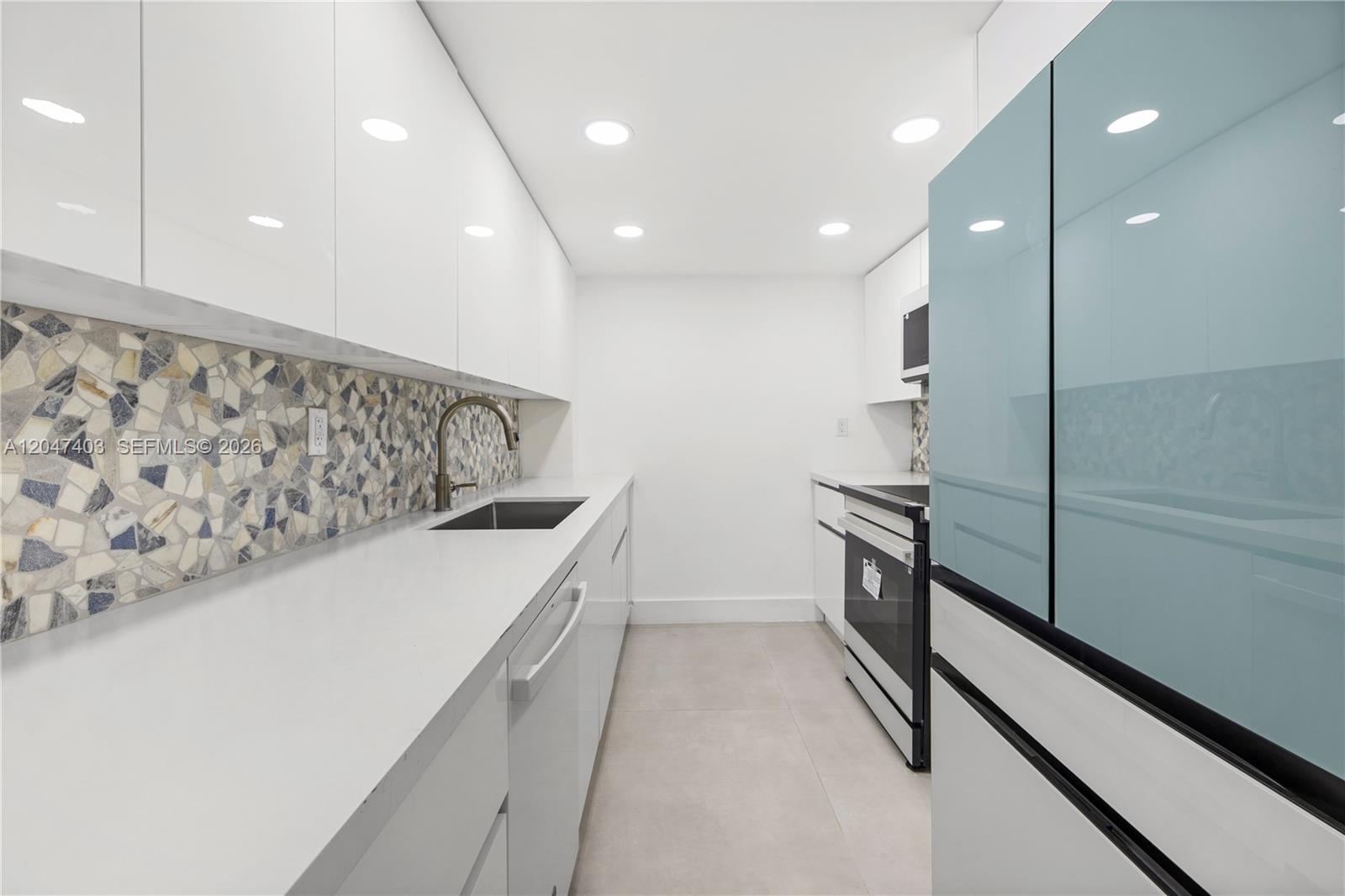 A galley kitchen features white cabinetry, a mosaic tile backsplash, and stainless steel appliances — 2457 Collins Ave # 201, Miami Beach FL 33140, MIAMI BEACH, FL