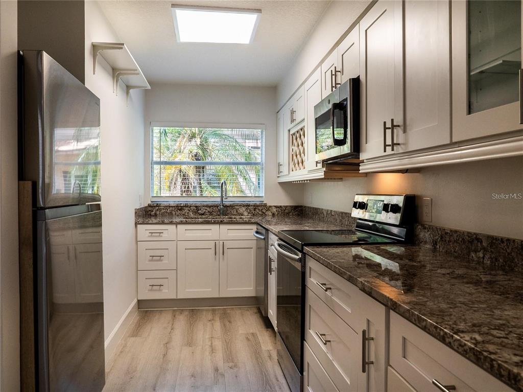 A galley kitchen features white cabinets, granite countertops, stainless steel appliances, and a window view — 517 S SUMMERLIN AVENUE, ORLANDO, FL