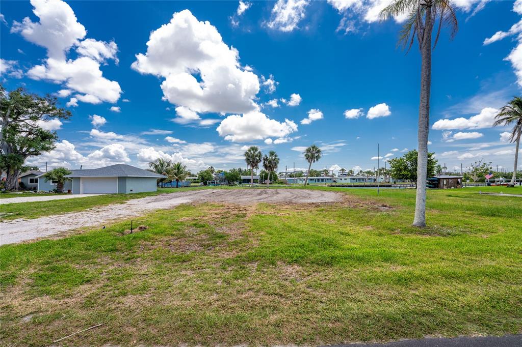 A vacant grassy lot with a gravel driveway and a nearby house under a blue sky — 1899 RIVERSIDE DRIVE, ENGLEWOOD, FL