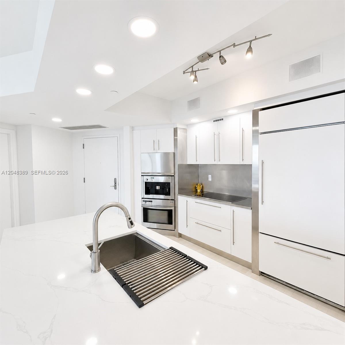 A modern white kitchen features a large island with a sink and stainless appliances — 450 Alton Rd # 1606, Miami Beach FL 33139, MIAMI BEACH, FL