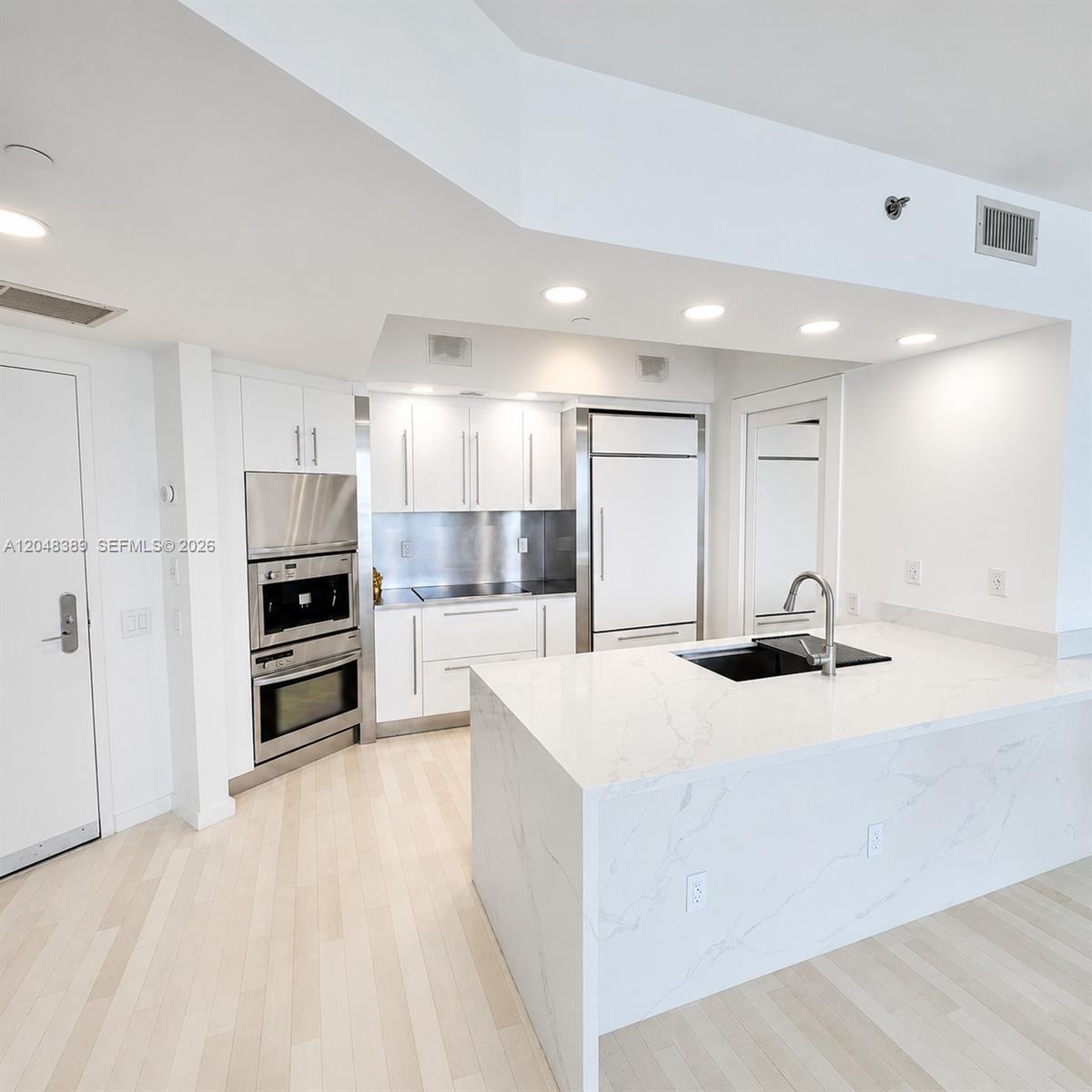 A modern kitchen features white cabinetry, stainless steel appliances, and a marble-topped island — 450 Alton Rd # 1606, Miami Beach FL 33139, MIAMI BEACH, FL