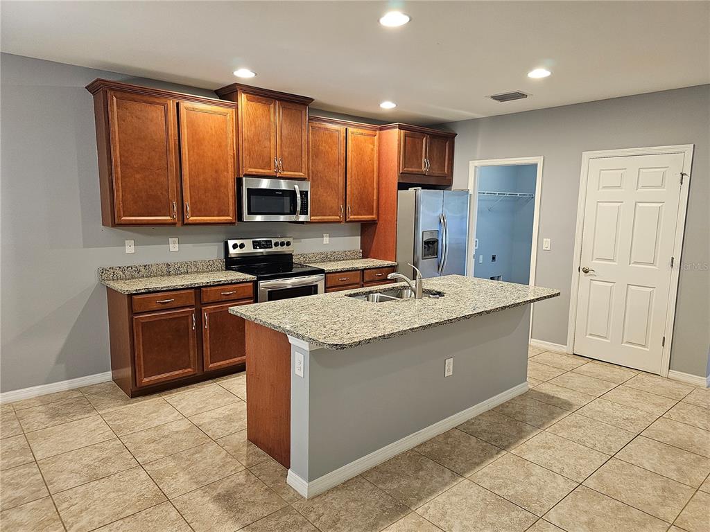 A kitchen features wood cabinets, granite countertops, a center island, and stainless steel appliances — 4266 DUTCHESS PARK ROAD, FORT MYERS, FL