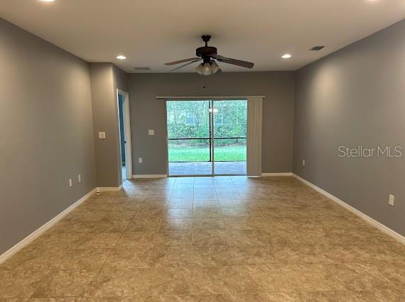 An empty living room with gray walls, tile flooring, a ceiling fan, and sliding glass doors — 4266 DUTCHESS PARK ROAD, FORT MYERS, FL