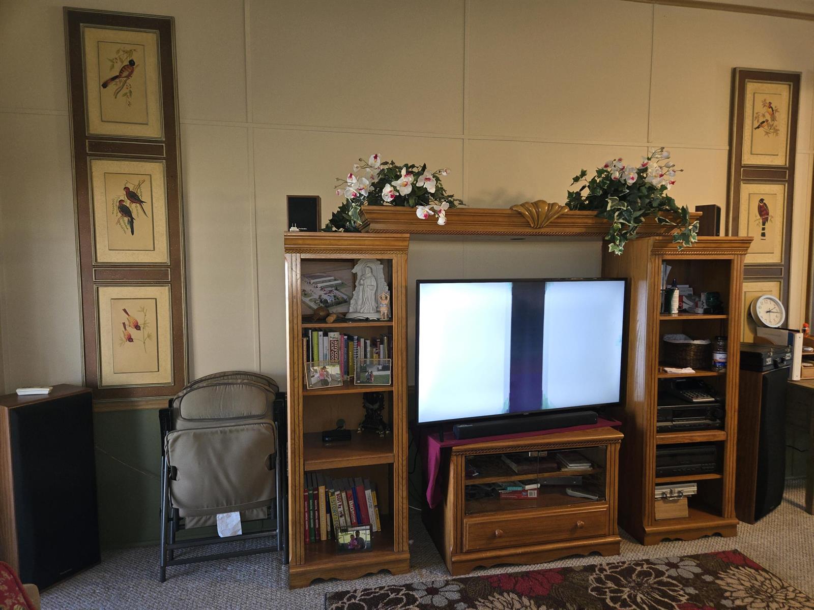 A living room features a wooden entertainment center with shelves, a television, and wall art — 14041 SE 126th Boulevard # 62, Okeechobee FL 34974, OKEECHOBEE, FL