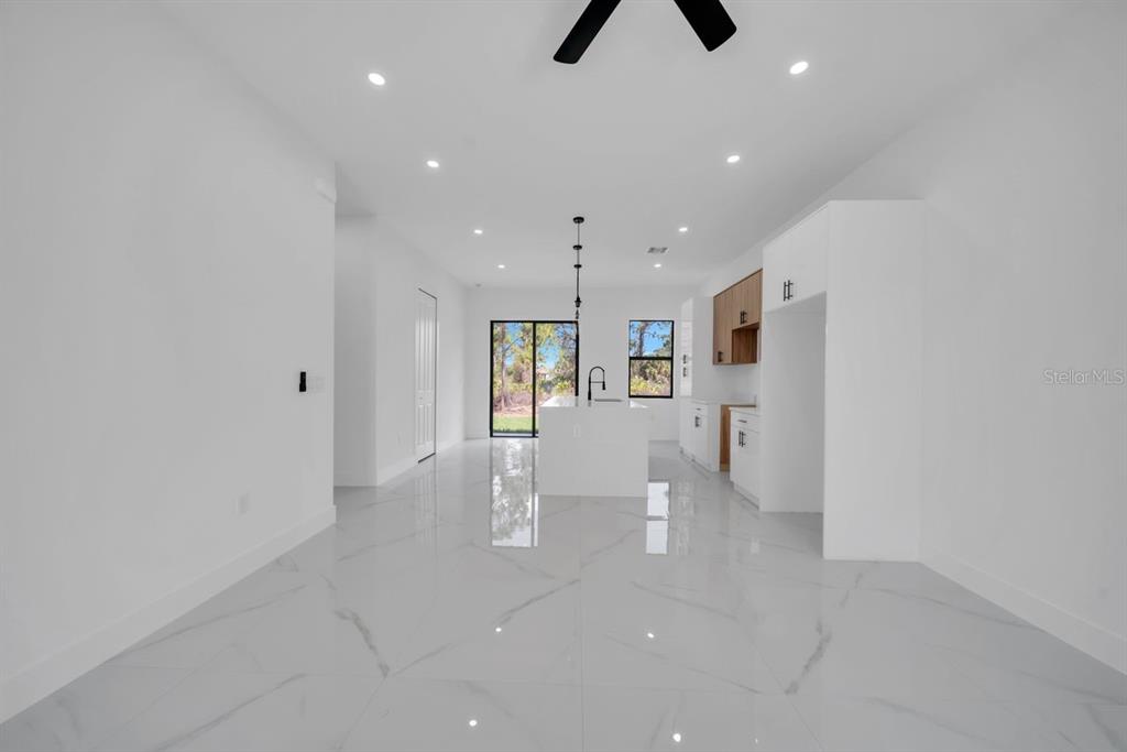 A bright, open-concept kitchen and living area features white marble-look tile floors and cabinetry — 637 SUMMIT AVENUE S, LEHIGH ACRES, FL