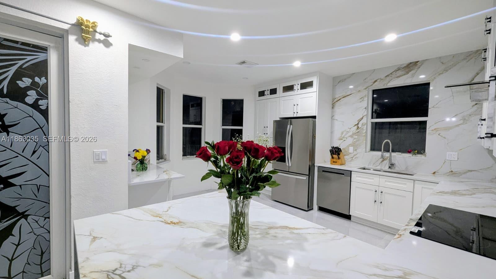 A modern kitchen features white cabinets, marble-patterned countertops, a stainless steel refrigerator, and red roses — 6049 SW 165th Ave, Miami FL 33193, MIAMI, FL