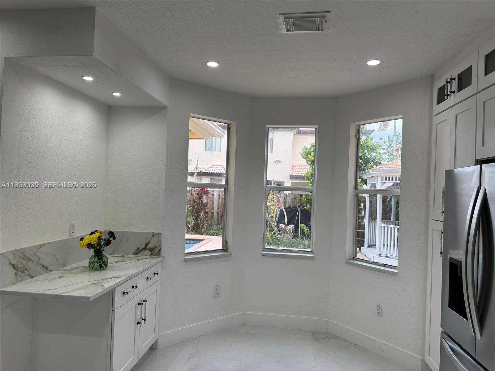 A kitchen breakfast nook features white cabinets, marble countertops, and three windows overlooking a pool — 6049 SW 165th Ave, Miami FL 33193, MIAMI, FL