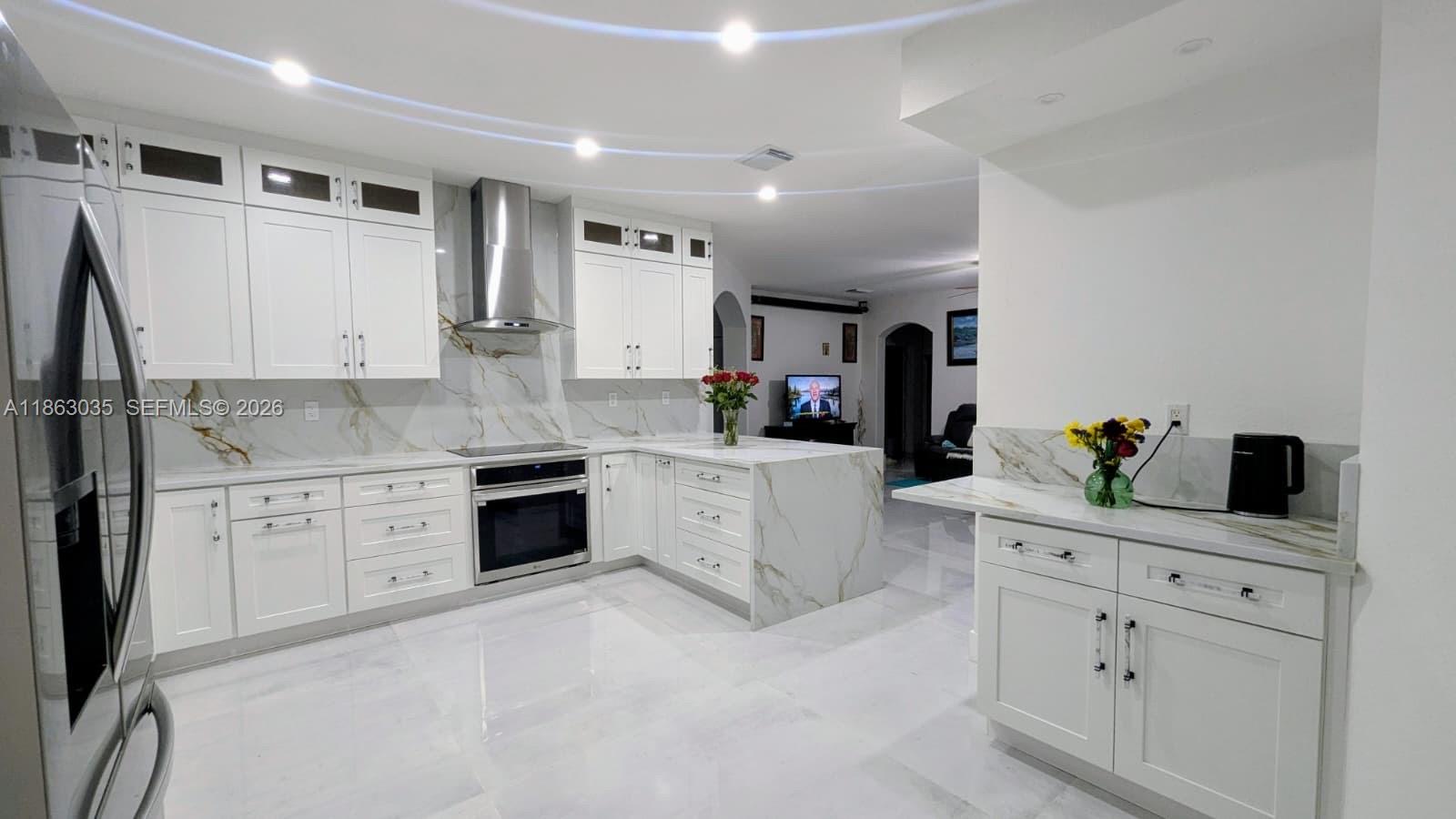 A modern white kitchen features marble countertops, a waterfall island, and stainless steel appliances — 6049 SW 165th Ave, Miami FL 33193, MIAMI, FL