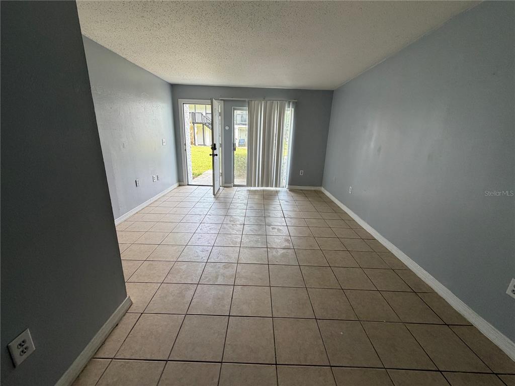 An empty room features light blue walls, beige tile flooring, and a sliding glass door — 4215 S SEMORAN BOULEVARD UNIT 15, ORLANDO, FL
