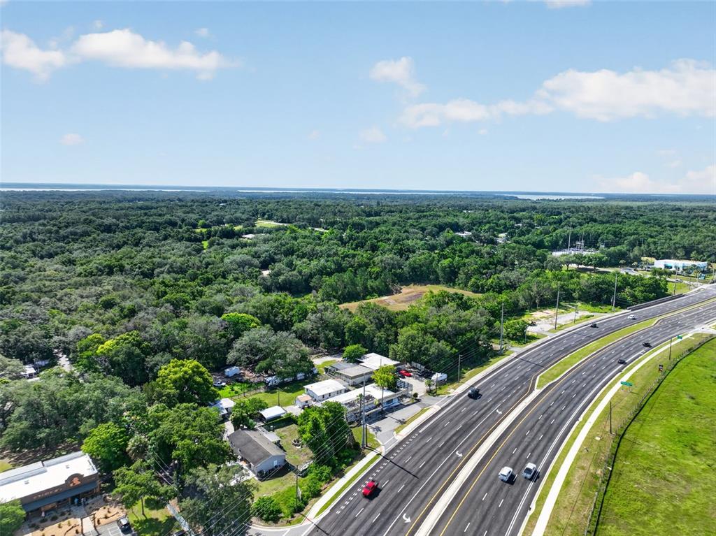 An aerial view shows a multi-lane highway running alongside a wooded area and buildings — 1945 S US HIGHWAY 441, LADY LAKE, FL