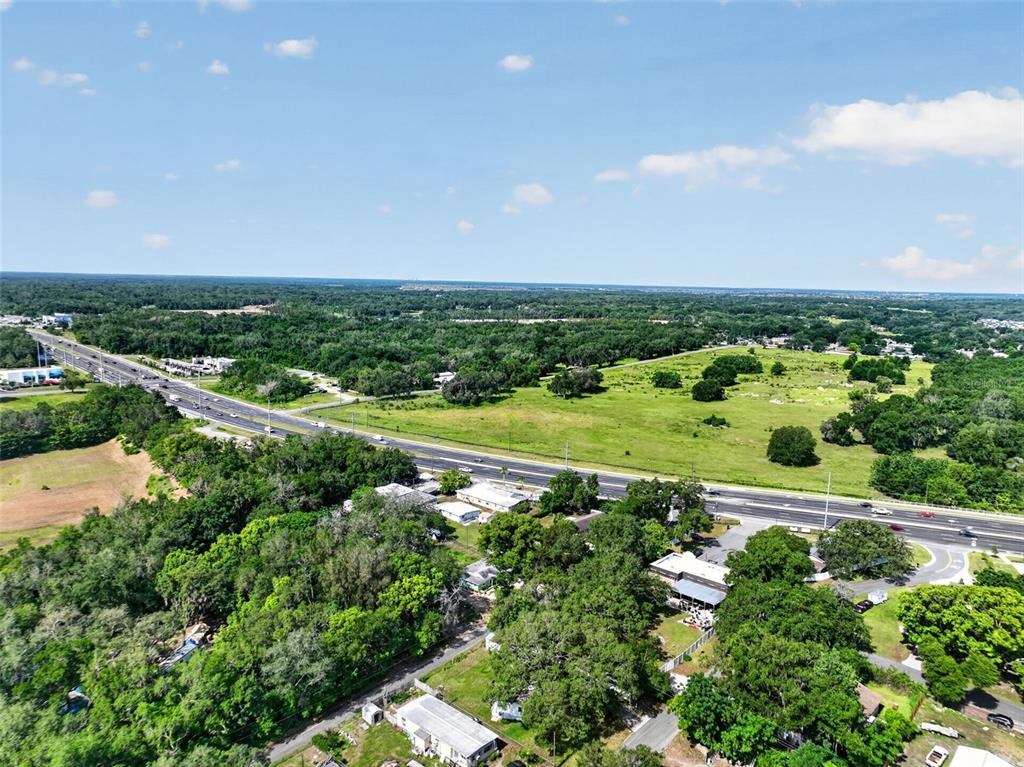 An aerial view shows a highway running through a landscape of trees and open fields — 1945 S US HIGHWAY 441, LADY LAKE, FL