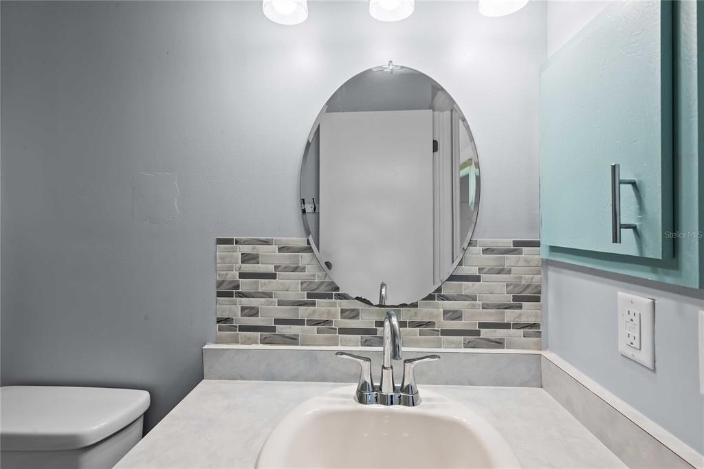 A bathroom vanity features a white sink, chrome faucet, oval mirror, and gray tiled backsplash — 348 CR 542E, BUSHNELL, FL