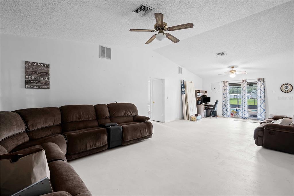 A spacious living room features a large brown sectional sofa, ceiling fans, and sliding glass doors — 348 CR 542E, BUSHNELL, FL