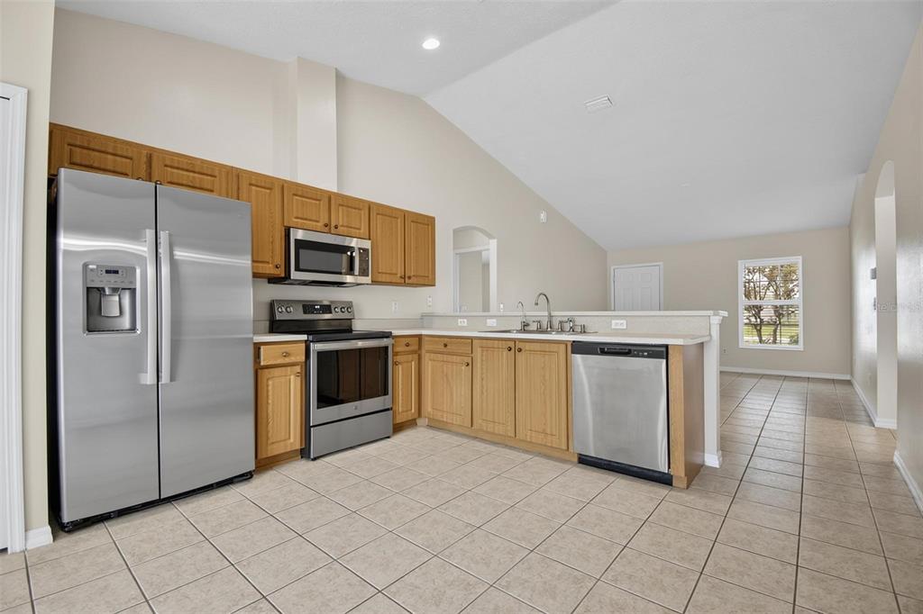 A kitchen with oak cabinets, stainless steel appliances, and tile flooring in an open floor plan — 83 LYNBROOK DRIVE UNIT A, PALM COAST, FL